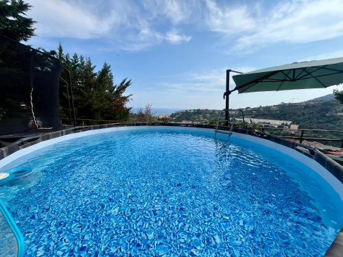 une grande piscine bleue avec un parasol dans l'établissement Villa à Menton avec vue mer, à Menton
