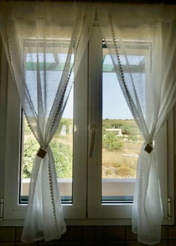 a window with white curtains and a view of a field at The Baker's Loft in Kýthira