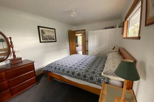a bedroom with a bed and a lamp and a dresser at Fully fenced, wrap around decks, water on 3 sides in Lunawanna