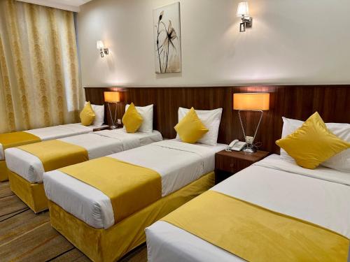 a hotel room with three beds with yellow pillows at VERTA Almahbas Hotel in Makkah