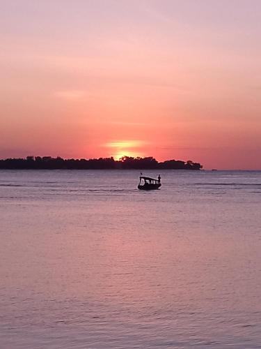 a boat in the water with a sunset in the background at Sea Breeze Villas - Gili Air, Lombok in Gili Air