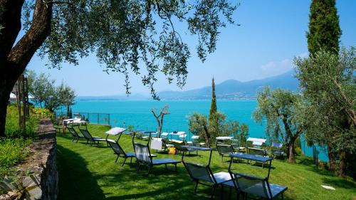 a row of chairs and tables on the grass near the water at Sky View Garda Lake by Hotel Galvani in Torri del Benaco