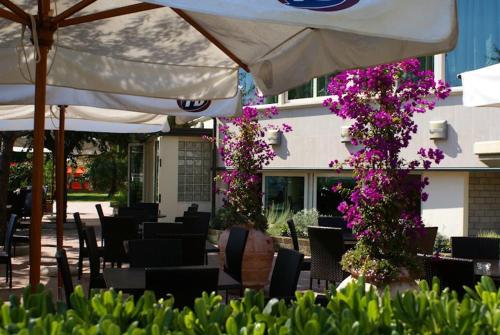 a patio with chairs and an umbrella and purple flowers at Hotel Lady Mary in Milano Marittima