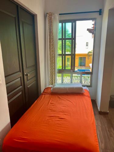 a bed with an orange blanket in a room with a window at Cancun-Soho in Cancún