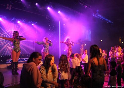 a group of women on a stage with purple lights at Golden Palm Resort in Chapel Saint Leonards