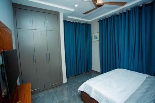 a bedroom with blue curtains and a bed and a tv at Gateway Lodge in Tamale