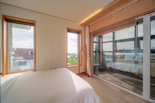 a bedroom with a white bed and large windows at Le Village Aewol building A in Jeju