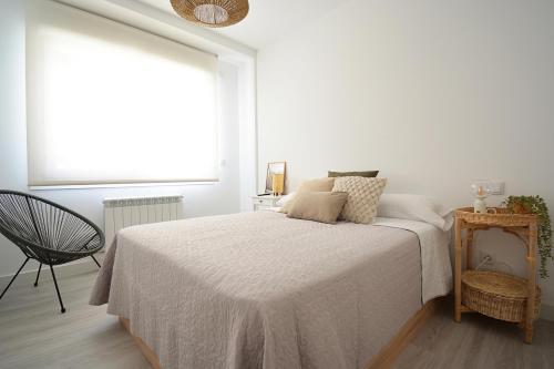 a white bedroom with a bed and a chair at GALIHOST - Apartamento en Playa de Compostela in Vilagarcia de Arousa