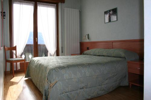 a bedroom with a bed and a chair and a window at Hotel Migliorati in Castione della Presolana
