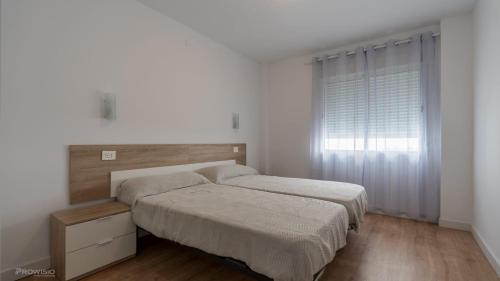 two beds in a white bedroom with a window at Apartamentos Borriana in Burriana