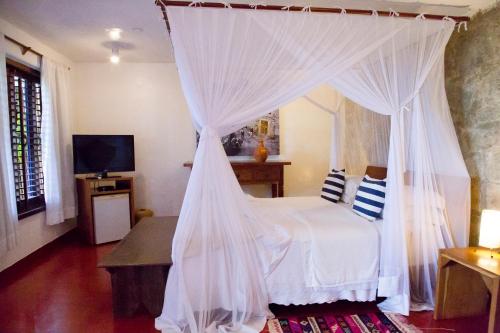 a bedroom with a canopy bed with white curtains at Pousada El Gordo in Trancoso