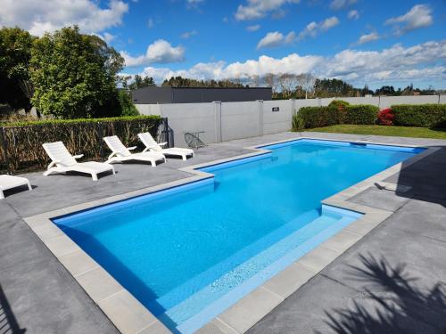 a swimming pool with lounge chairs next to a fence at JetPark Hamilton Airport New Zealand in Hamilton
