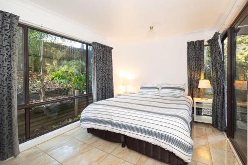 a bedroom with a bed and a large window at Valley Hideaway - Whole House in Narrawallee