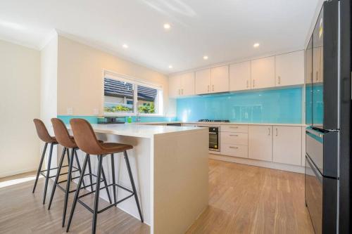 a kitchen with white and blue cabinets and bar stools at Three-Bedroom Home in Somerville in Auckland