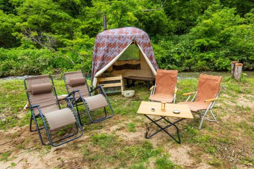 a group of chairs and a tent in the grass at Yamanomura Campsite in Hida