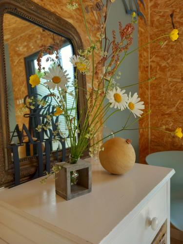 un vase de fleurs sur une commode devant un miroir dans l'établissement Lodge au vent, à Savigné-lʼÉvêque