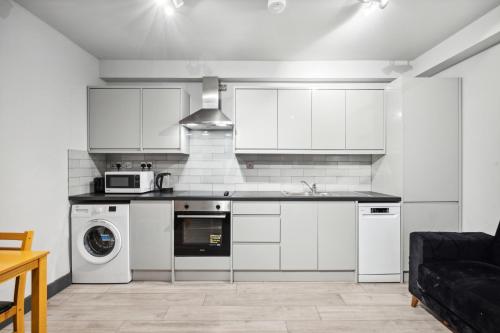 a kitchen with white cabinets and a washer and dryer at Cozy London Apartment in London