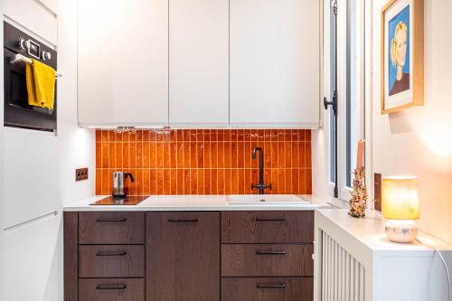 - une cuisine avec des placards blancs et un mur en carrelage orange dans l'établissement GuestReady - Bright Apt near Sacré-Coeur, à Paris