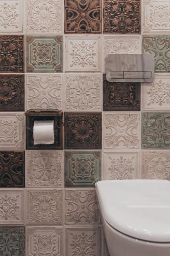 a bathroom with a toilet and a tiled wall at Lindens apartments with AC and view to central square in Panevėžys