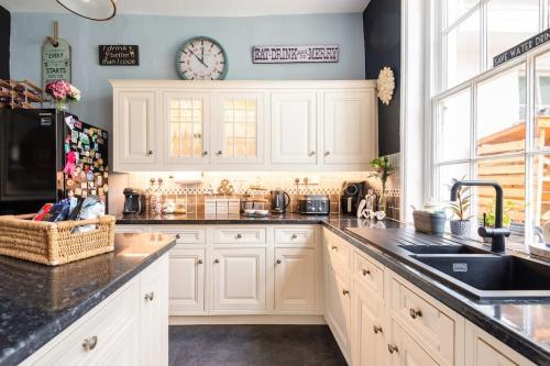a kitchen with white cabinets and a clock on the wall at Uplands House Tewkesbury in Tewkesbury