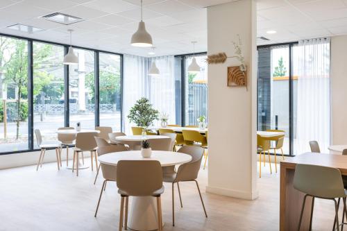 une salle à manger avec tables, chaises et fenêtres dans l'établissement Oh Activ Nîmes, à Nîmes