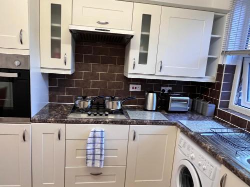 a kitchen with white cabinets and a stove top oven at Abbey Wood Serviced Apartment 3BRH Free Wi-Fi Parking Tea and Coffee in Belvedere