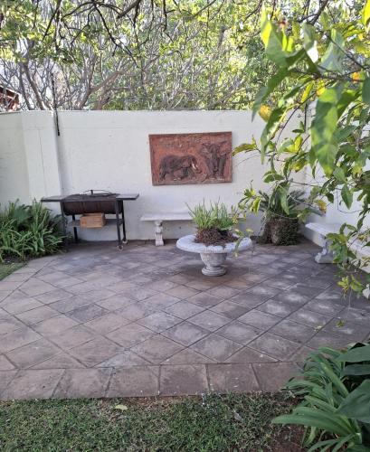 a patio with a bench next to a white wall at Big Tree Guesthouse Brits in Brits