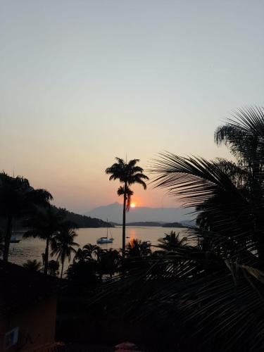 a sunset over the water with a palm tree at Pousada Éden in Angra dos Reis