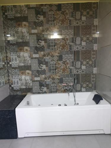 a white bath tub in a bathroom with a tile wall at RKS INTERNATIONAL HAMPi in Hampi