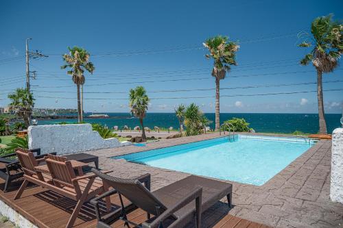 a swimming pool with chairs and the ocean in the background at Le Village Aewol G in Jeju