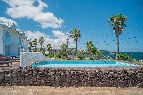 a swimming pool with a stone wall and palm trees at Le Village Aewol G in Jeju