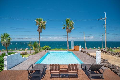 a swimming pool with chairs and the ocean in the background at Le Village Aewol F in Jeju