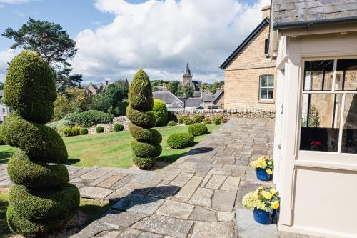 a garden with a row of trees and a house at Dun Brae Cottage in Dornoch
