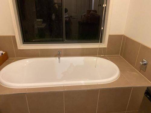 a bath tub sitting under a window in a bathroom at Family home close to Melb Airport, free FAST WIFI! in Craigieburn