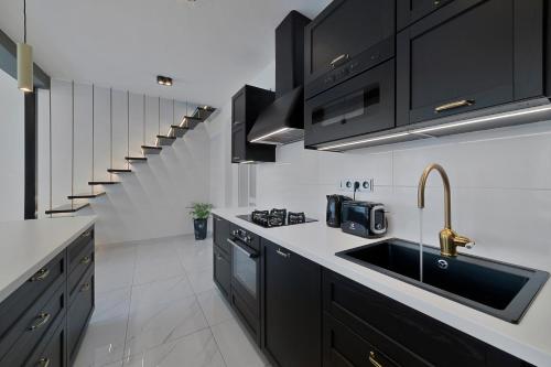 a kitchen with black cabinets and a sink and a staircase at Boutique Apartment Owned by Emperor Peter The Great With 2 Balconies & Jacuzzi in Karlovy Vary