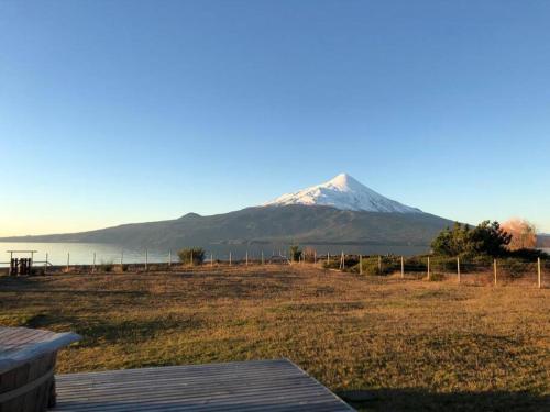 a snow covered mountain in the distance with a field at Espectacular casa orilla de lago in Puerto Varas