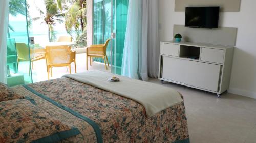 カマサリにあるCasa Frente Mar 5 Suítes Guarajuba em Condomínioのベッドとテレビとバルコニーのある寝室