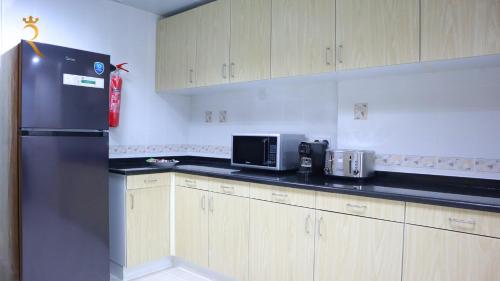 a kitchen with a black refrigerator and wooden cabinets at Al Raha 3BR Retreat - Stylish Family Escape in Abu Dhabi