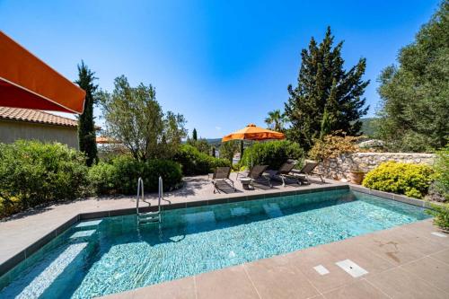 a swimming pool with chairs and an umbrella at North Point Houses in Fiskardho