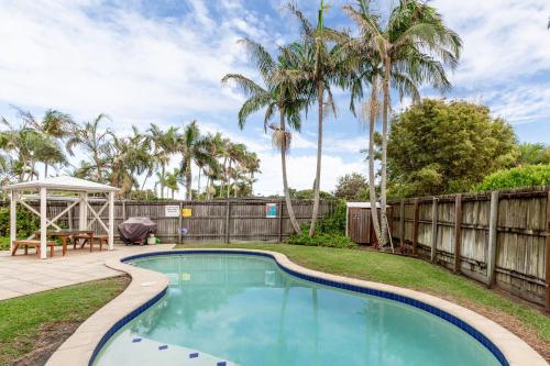 a swimming pool in a yard with a fence and palm trees at Marcoola Sands Retreat Steps from Marcoola Beach in Marcoola