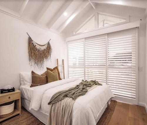 a white bedroom with a large bed and a window at The Hamptons House Kiama in Kiama