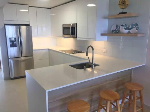 a white kitchen with a sink and two bar stools at Villa Brisas del Mar-Ocean View, Gated Community in Dorado