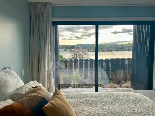 a bedroom with a bed and a large glass window at Lakefront Living - Lake Rotoiti Holiday Home in Rotorua