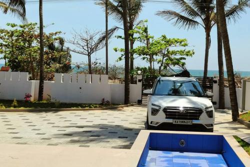 a white car parked in a driveway with palm trees at Sunset Bay Beach Villa in Mangalore