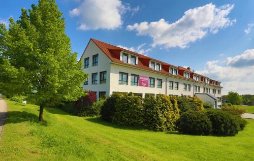 a building with a red roof on a green field at Hotel Sportwelt Radeberg in Radeberg