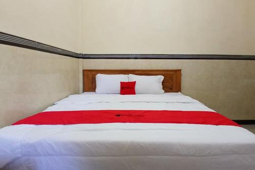 a large white bed with a red blanket on it at RedDoorz at Dien Homestay Syariah Alun-alun Pasuruan in Krampijangan