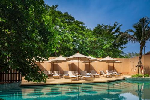 a swimming pool with lounge chairs and umbrellas at The Proud Karon Beach Phuket Trademark Collection By Wyndham in Karon Beach