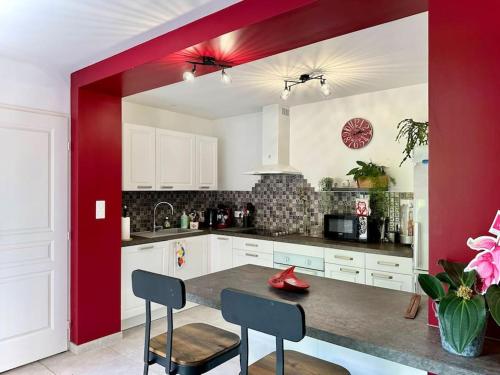 une cuisine avec des placards blancs et un mur rouge dans l'établissement La terrasse fleurie, à Salies-du-Salat