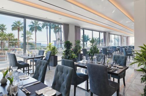 a restaurant with tables and chairs and large windows at St George Beach Hotel & Spa Resort in Paphos
