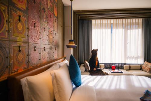 a hotel room with a bed and a woman sitting in a window at Hotel Indigo Jiuzhai by IHG in Jiuzhaigou